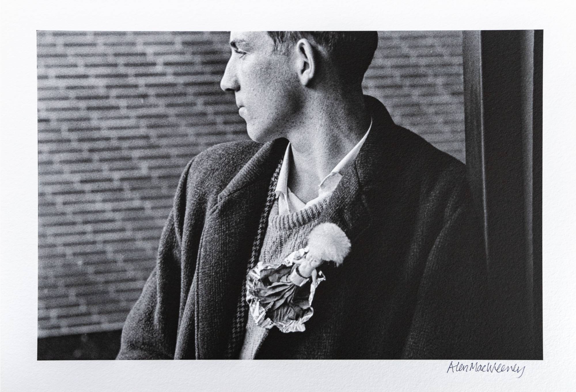 young man in black coat looking out the window wearing doll brooch